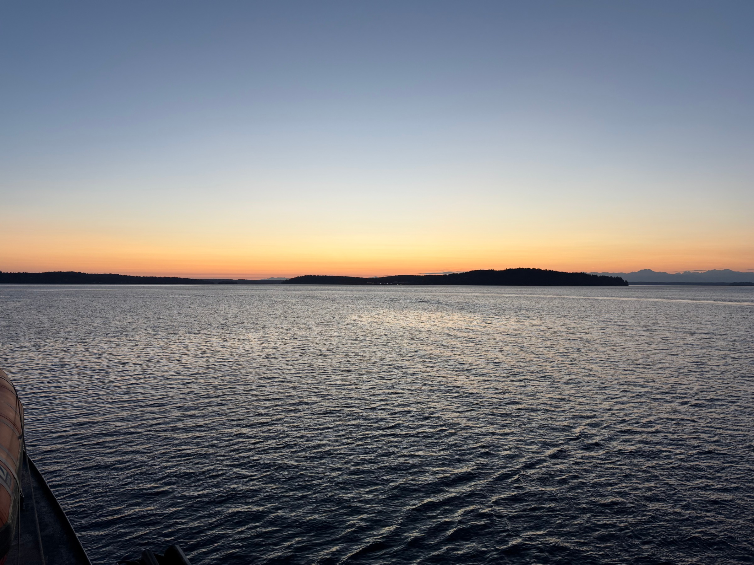 The last orange light of sunset beyond dark island silhouettes, seen across gently rippled water from the evening ferry.